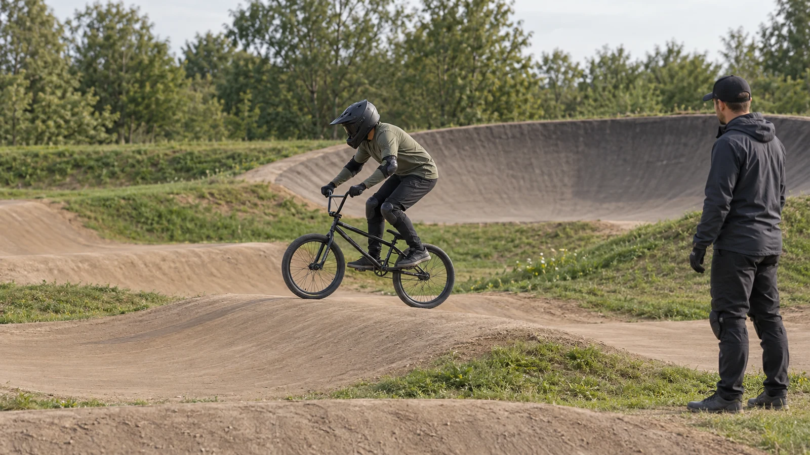 Новичок в защитной экипировке проходит низкий роллер на учебной BMX-трассе